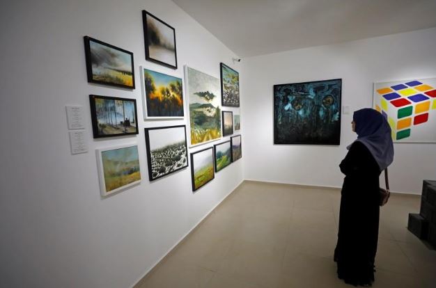 زائرة تقف أمام لوحات بمعرض لشبان فلسطينيين في البيرة بالضفة الغربية يوم الثلاثاء. تصوير: محمد تركمان - رويترز